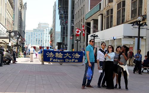 来自德国的Ceyda（中）和她的几个朋友来到渥太华旅游，正好遇到天国乐团游行，他们就走在乐团的前面一直用手机自拍和天国乐团一起行进的情景