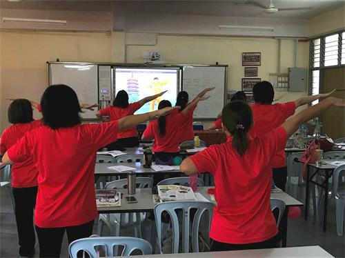 '图2：二零一八年七月十八日，学校老师们跟随教功录像学法轮大法第一套功法'