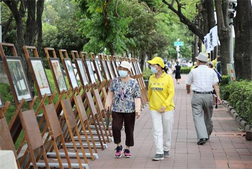 图3: 李姓学员陪着对大法有误解的老太太，边走边看展板，经过学员细心讲真相之后，老太太心中豁然开朗，解开心中的误解。